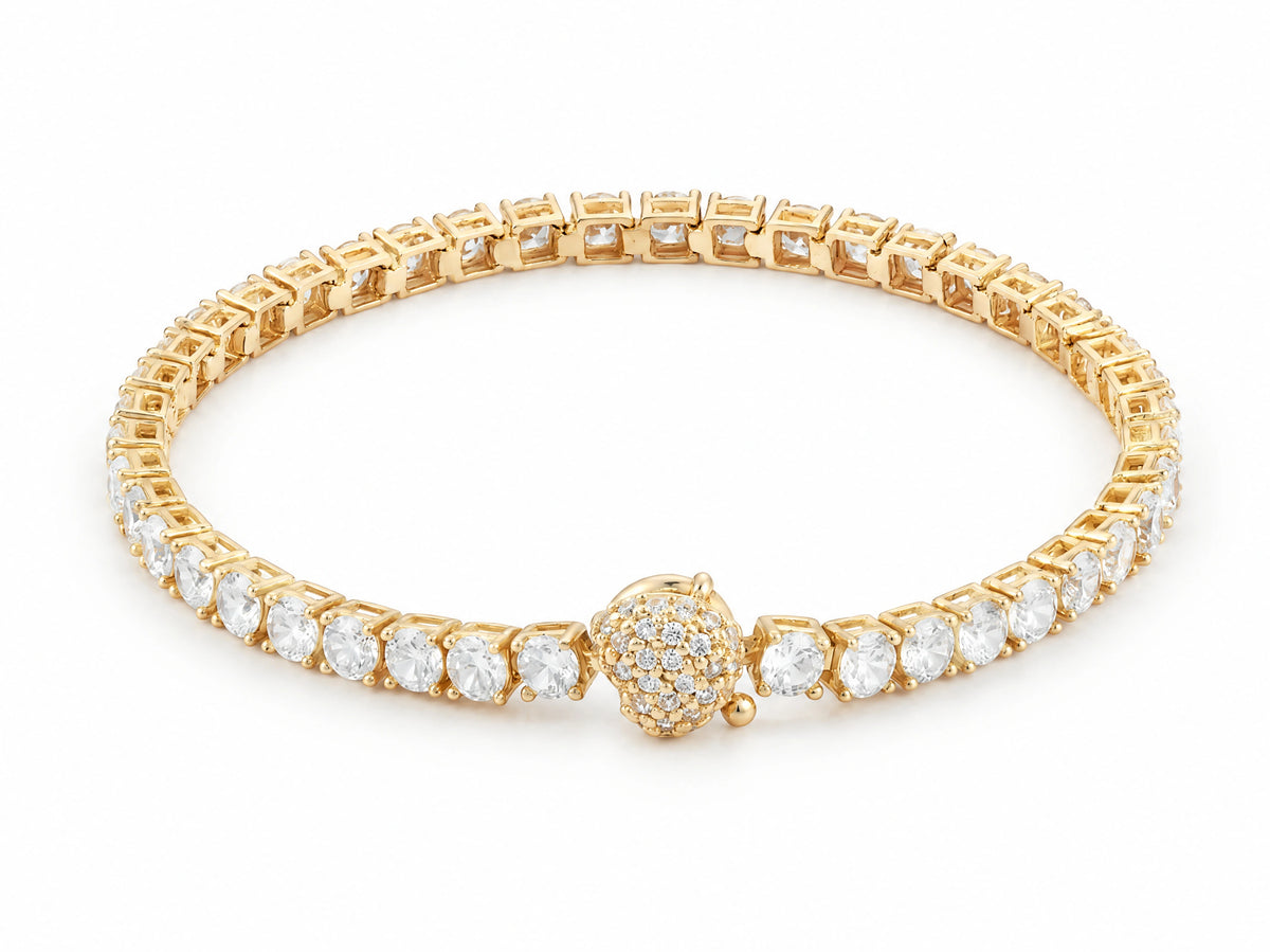 18K yellow gold zirconia tennis bracelet laid in a closed circle on white, one continuous row of round stones in four-prong settings, the pave-set spherical clasp at the front