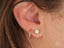 Close-up of a woman’s ear with Glimmergold 18k Mini Hoops and diamond stud earrings