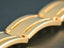 A gold-colored metal bracelet with distinct curved links and decorative grooves.
