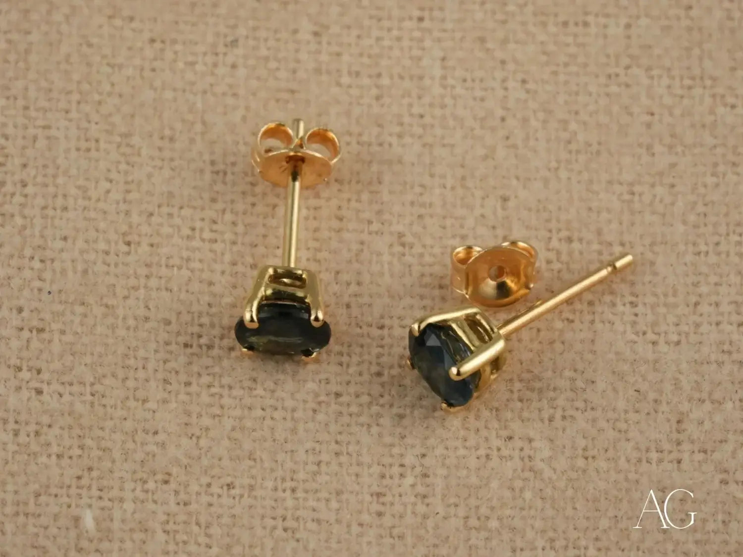 Gold-tone stud earrings with dark blue gemstones in a four-prong setting showcasing luxury jewelry and fine gold jewelry craftsmanship.