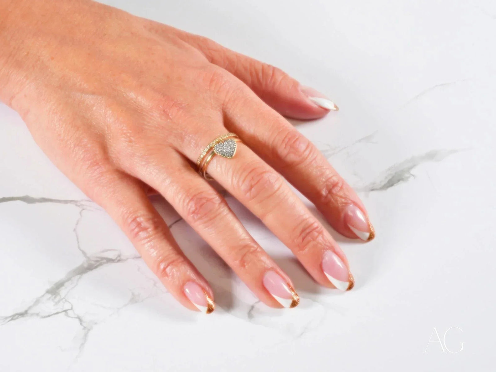 Womans hand with Heart’s Glow Ring, French tip manicure and radiant 18k gold heart charm