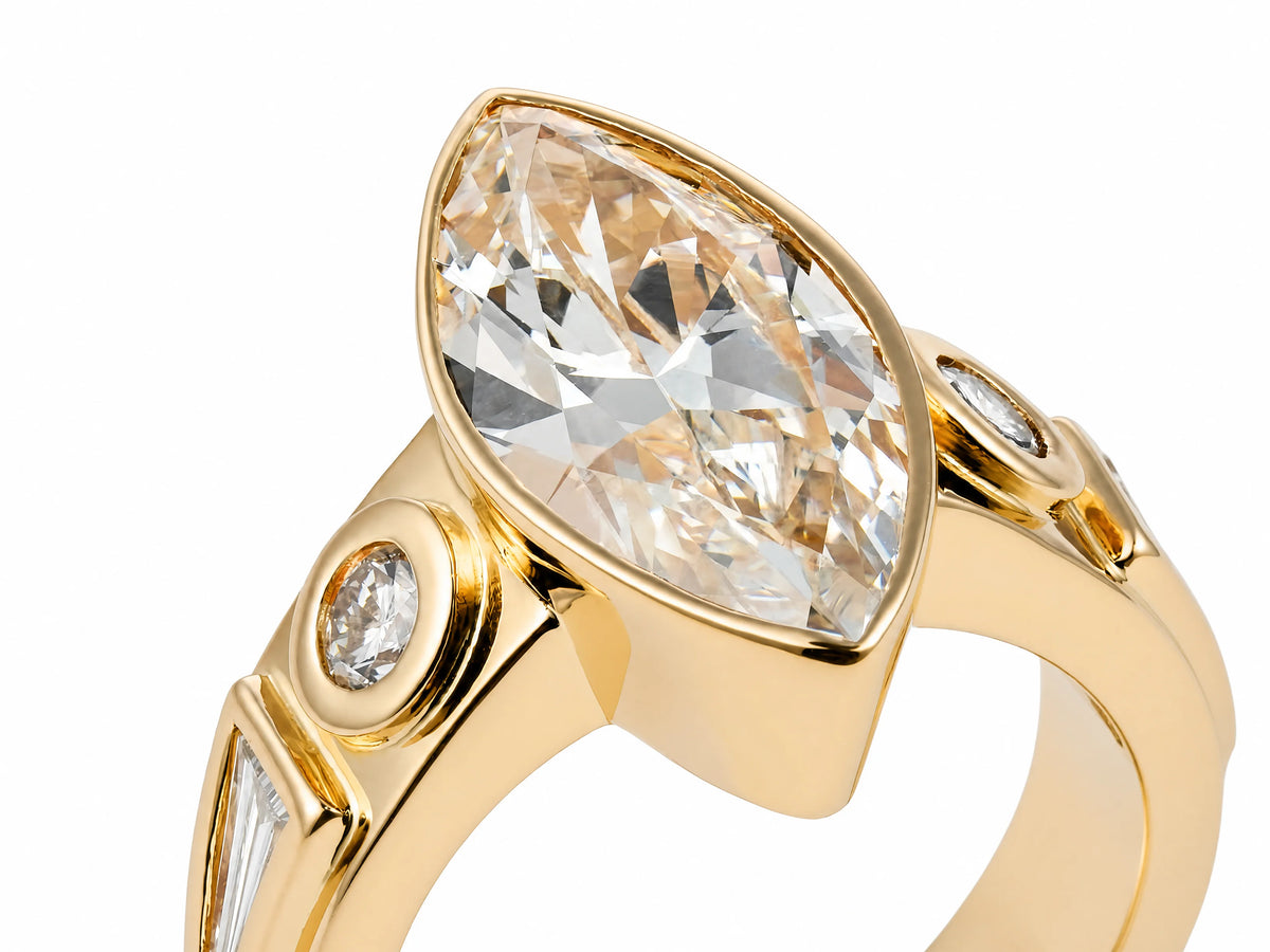 Marquise diamond ring in yellow gold bezel with round accent stone, angled close-up showing faceting and setting details
