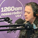 Middle-aged man wearing headphones and a leather jacket, speaking into a microphone in a radio studio.