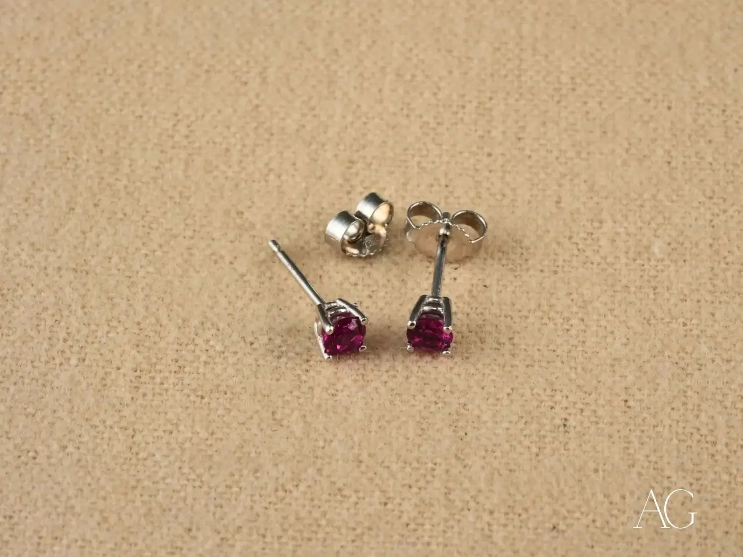 A pair of elegant stud earrings featuring vibrant red rubies set in sleek silver metal with four-prong settings illustrating fine jewelry and the cultural roles of art gold in ancient civilizations.