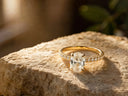 A radiant oval-cut diamond engagement ring set in a yellow gold band adorned with smaller diamonds along its sides.