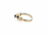 Side profile of two-tone gold ring showing sculpted hand forms and sapphire setting