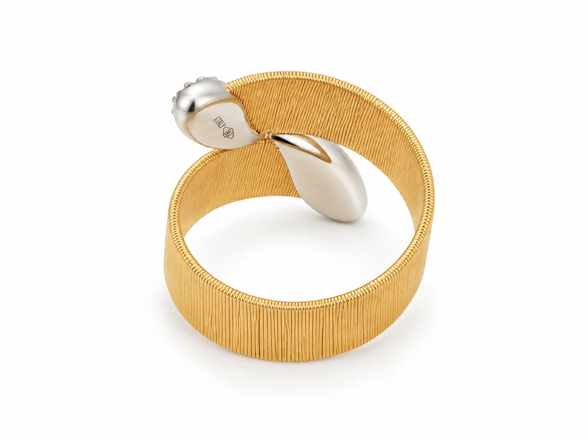 Angled top view of the two-tone ring; the white gold ribbon crosses the brushed yellow gold band, widening into two rounded lobes; ITALY marking visible inside the shank.