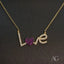 Gold-plated ’Love’ necklace with a heart charm encrusted with purple stones and the letters ’L’ and ’E’ encrusted with clear stones.