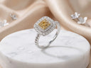 A stunning square-cut yellow diamond ring, surrounded by a halo of sparkling white diamonds and set in an elegant silver band with twisted detailing.