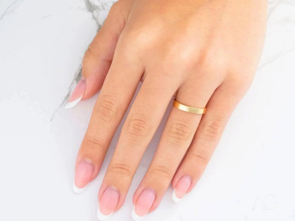 18k yellow gold wedding band on hand with French-tipped nails