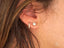 Ear adorned with 18k yellow gold mini hoops earrings and diamond studs in art gold jewelry style