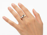 Top-down view of two-tone gold ring with clasped hands holding sapphire, diamond details visible