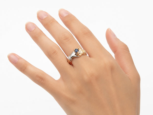 Top-down view of two-tone gold ring with clasped hands holding sapphire, diamond details visible