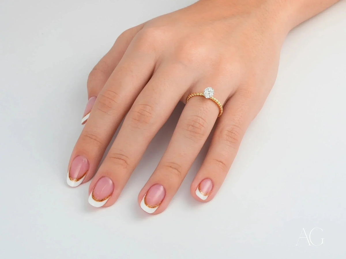 Hand with French-tipped nails wearing Twist of Brilliance twisted band engagement ring featuring diamond focal point
