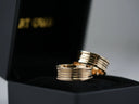 Two gold-toned wedding bands with a sleek, multi-layered design rest elegantly in a black velvet box.