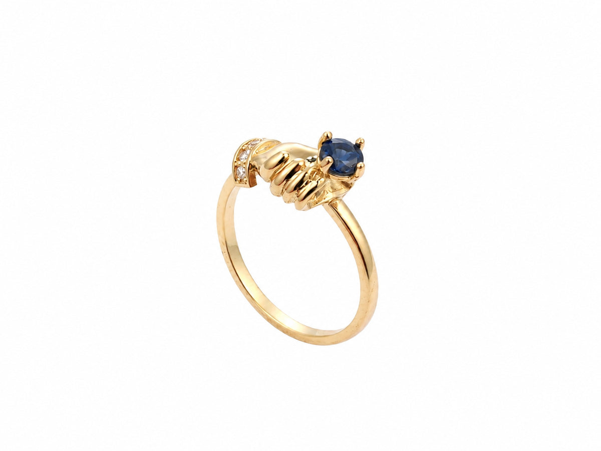 Side view of white gold ring with sculpted hands, diamond cuff and sapphire detail