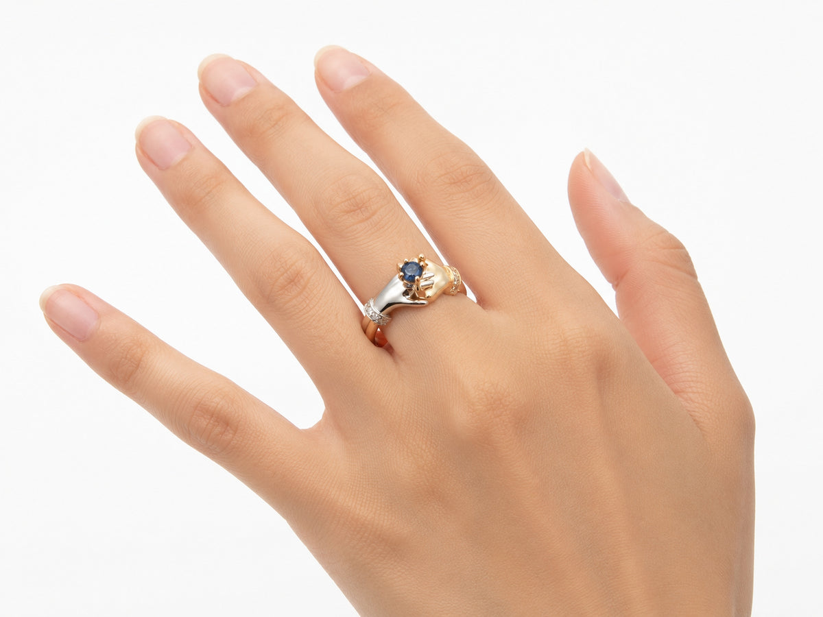 Top-down view of two-tone gold ring with clasped hands holding sapphire, diamond details visible