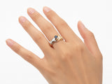 Top-down view of two-tone gold ring with clasped hands holding sapphire, diamond details visible