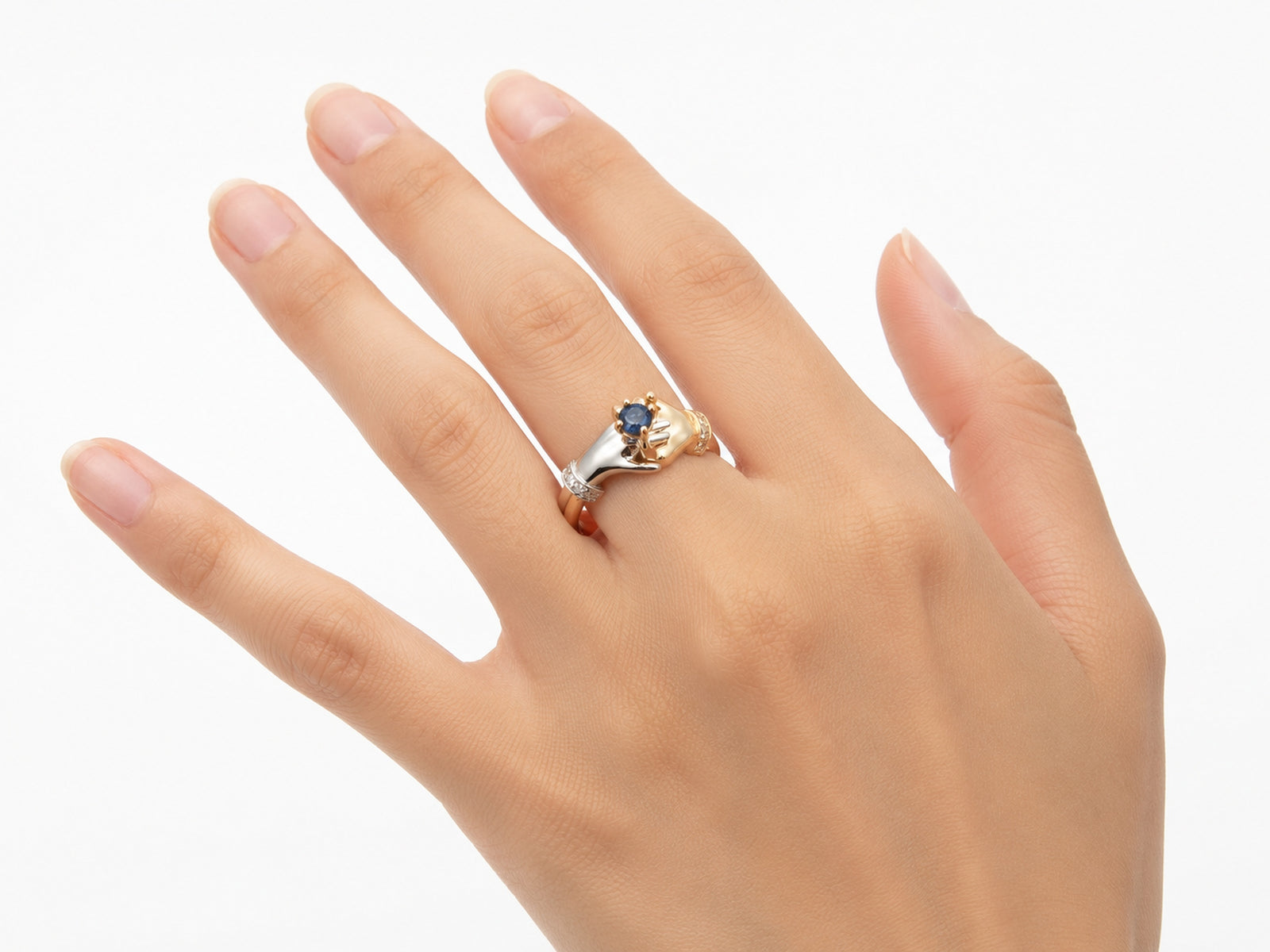 Top-down view of two-tone gold ring with clasped hands holding sapphire, diamond details visible