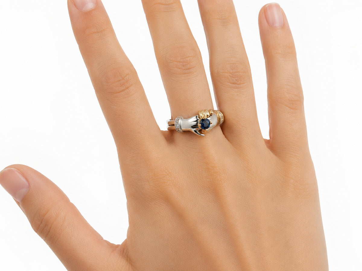 Three-quarter view of two-tone gold ring with clasped hands, sapphire and diamond cuff details