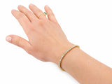 The tennis bracelet on a wrist seen from the back of the hand, with a gold ring set with a green stone on one finger